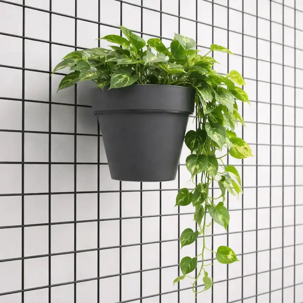 Vaso con pianta verde appeso a una griglia loft in metallo mediante un supporto per vaso.